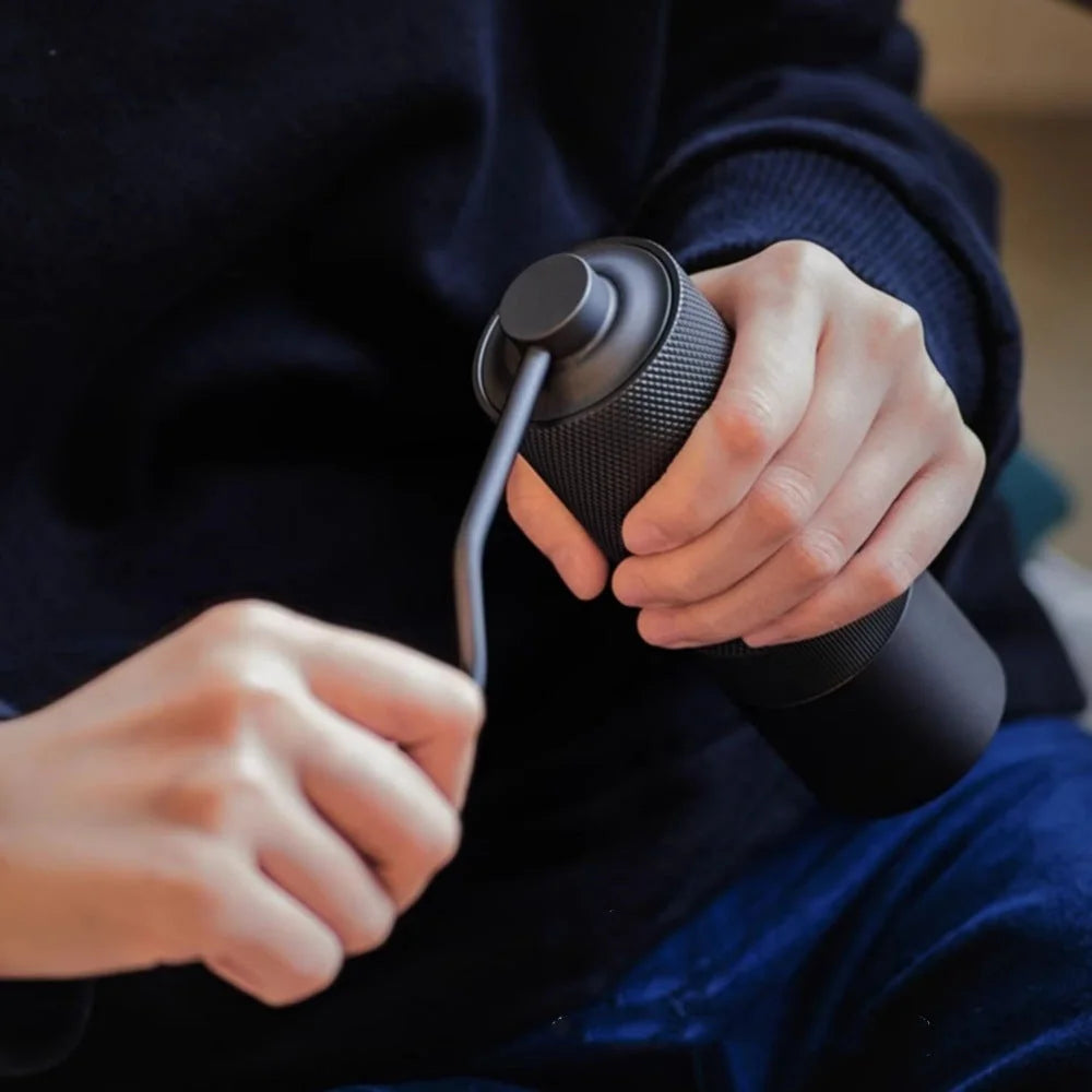 Close-up of hands grinding coffee with the black MAVO Wizard 2.0, knurled anti-slip aluminium body