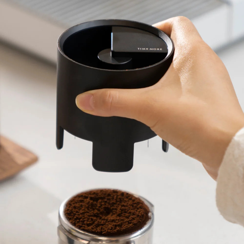 A hand holding the black Autospin WDT Tool just above a portafilter basket filled with ground coffee