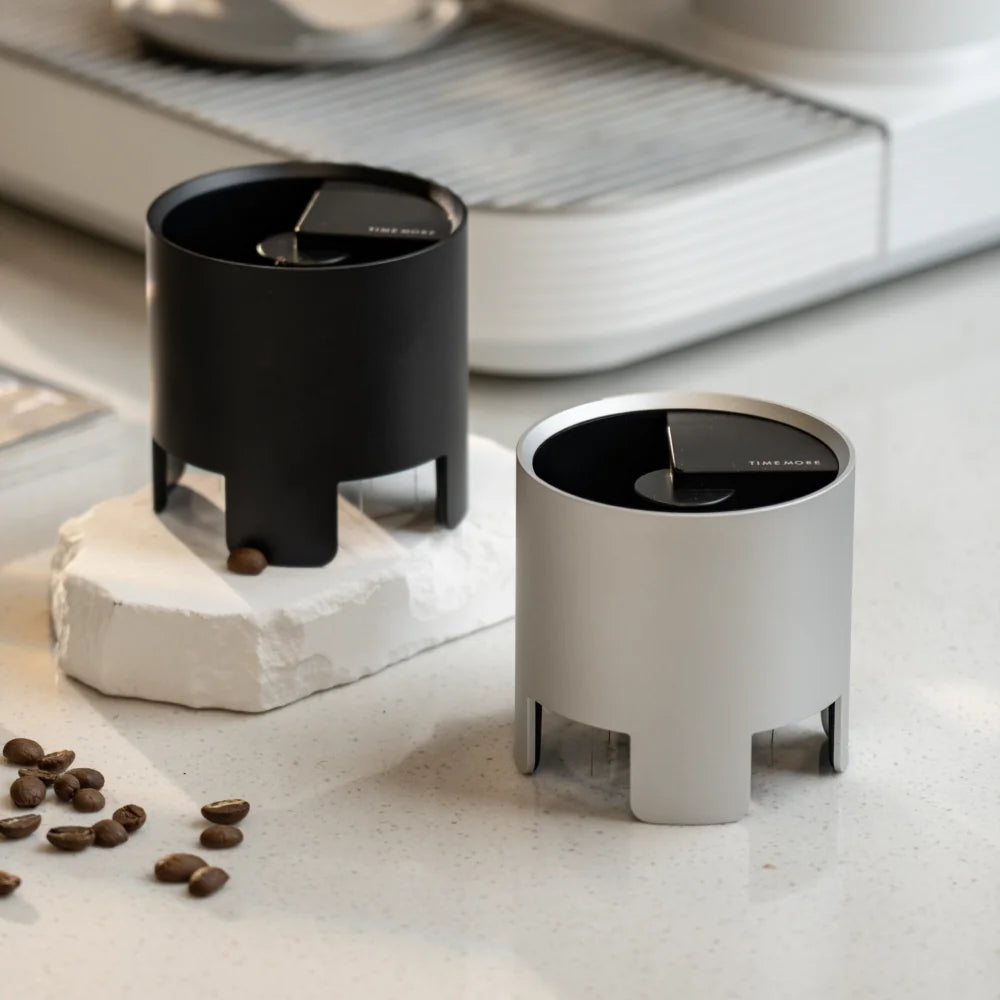 The black and silver Autospin WDT Tools side by side on a white stone slab with coffee beans scattered around
