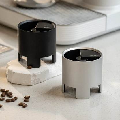 The black and silver Autospin WDT Tools side by side on a white stone slab with coffee beans scattered around