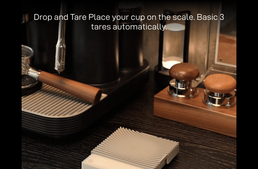Drop and Tare: a glass cup placed on the white Basic 3 on an espresso machine drip tray — 'Place your cup on the scale. Basic 3 tares automatically.'