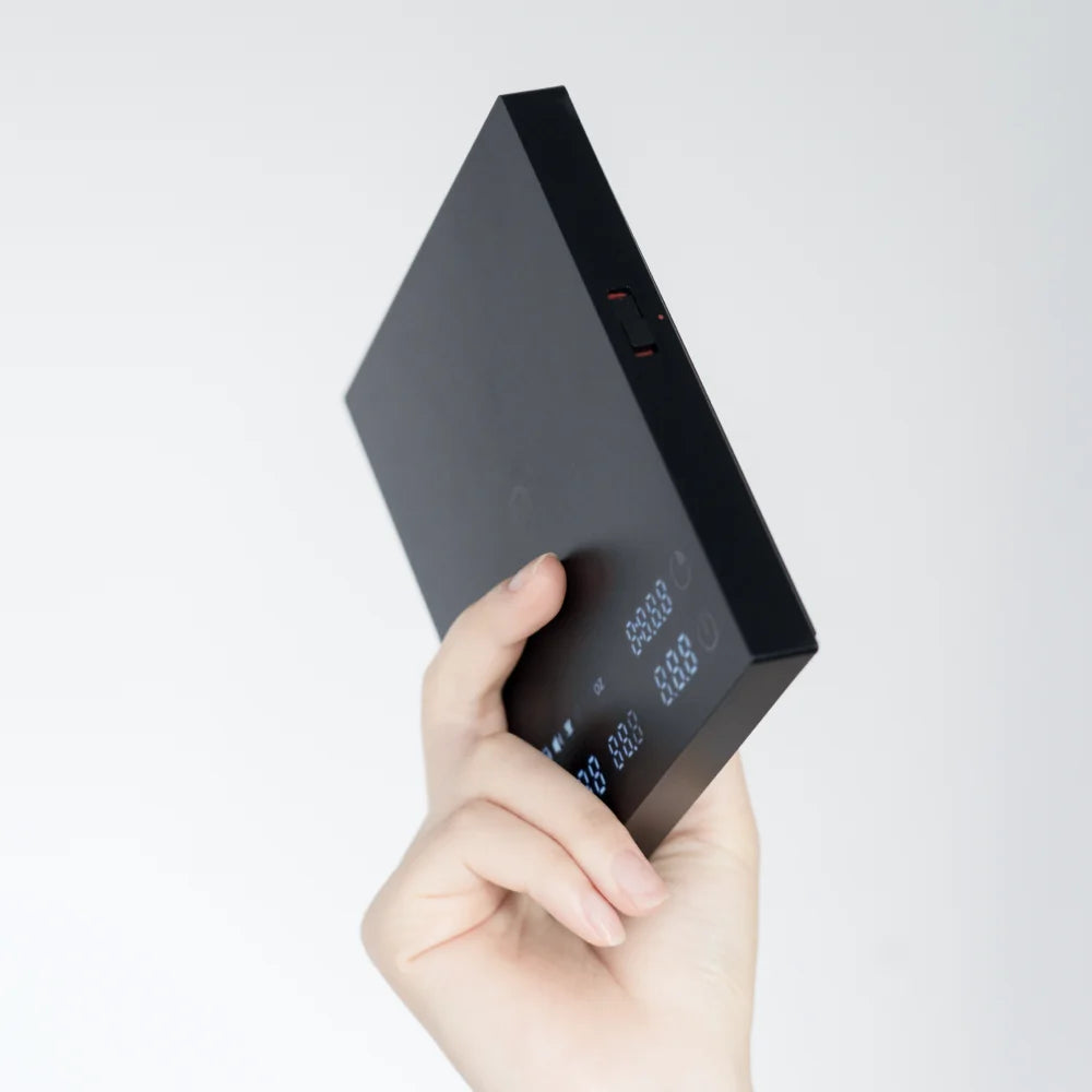 A hand holding the bare black TIMEMORE Basic 3 edge-on, showing how thin and light the 300g chassis is
