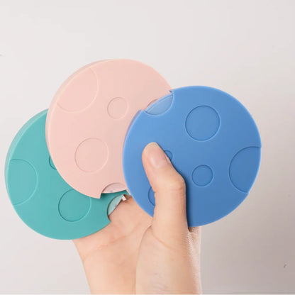 A hand holding a fan of pink, blue and teal TIMEMORE Dot silicone mats, each with a pattern of round craters