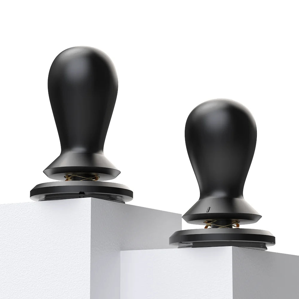 Two FLOW tampers standing on white plinths, each with a gold wave spring visible between the collar and the base
