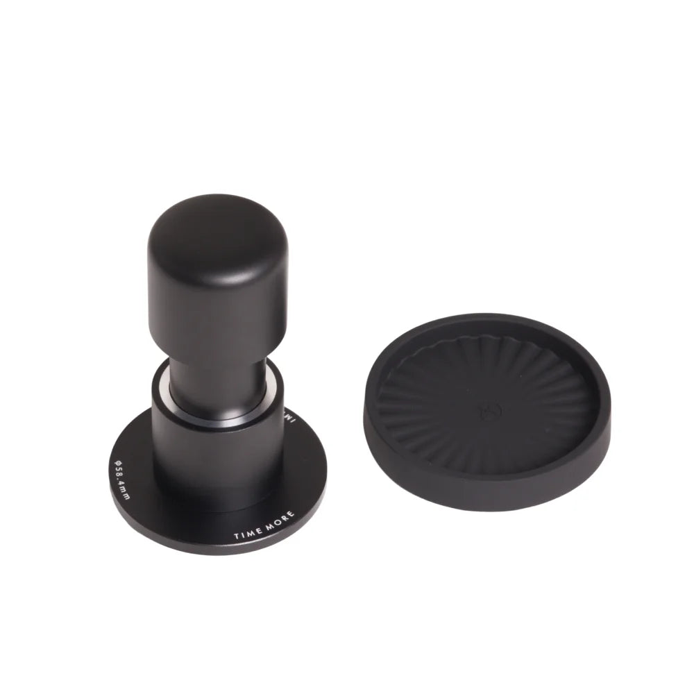 TIMEMORE Impulse Impact Tamper standing on its 58.4mm base beside its round ribbed silicone base on a white background