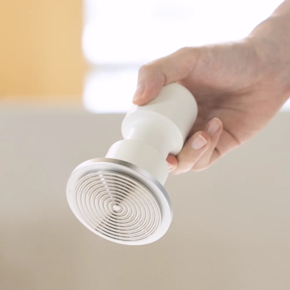 A hand holding the white Impulse Impact Tamper with its concentric ripple base turned towards the camera