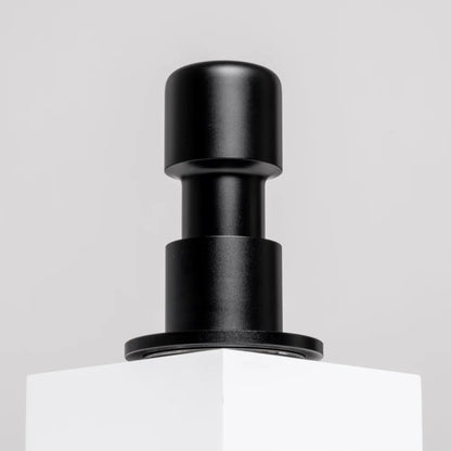 Black Impulse Impact Tamper standing on a white plinth against a light grey wall