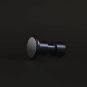Black Impulse Impact Tamper lying on its side on a dark surface with its flat 58.4mm base facing the camera