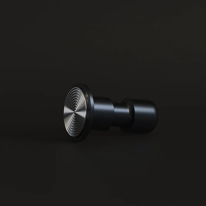 Black Impulse Impact Tamper lying on its side on a dark surface with its concentric ripple 58.4mm base facing the camera