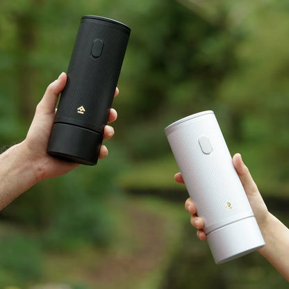 Two hands holding a black and a light-coloured TIMEMORE x MILLAB E01 grinder outdoors among trees