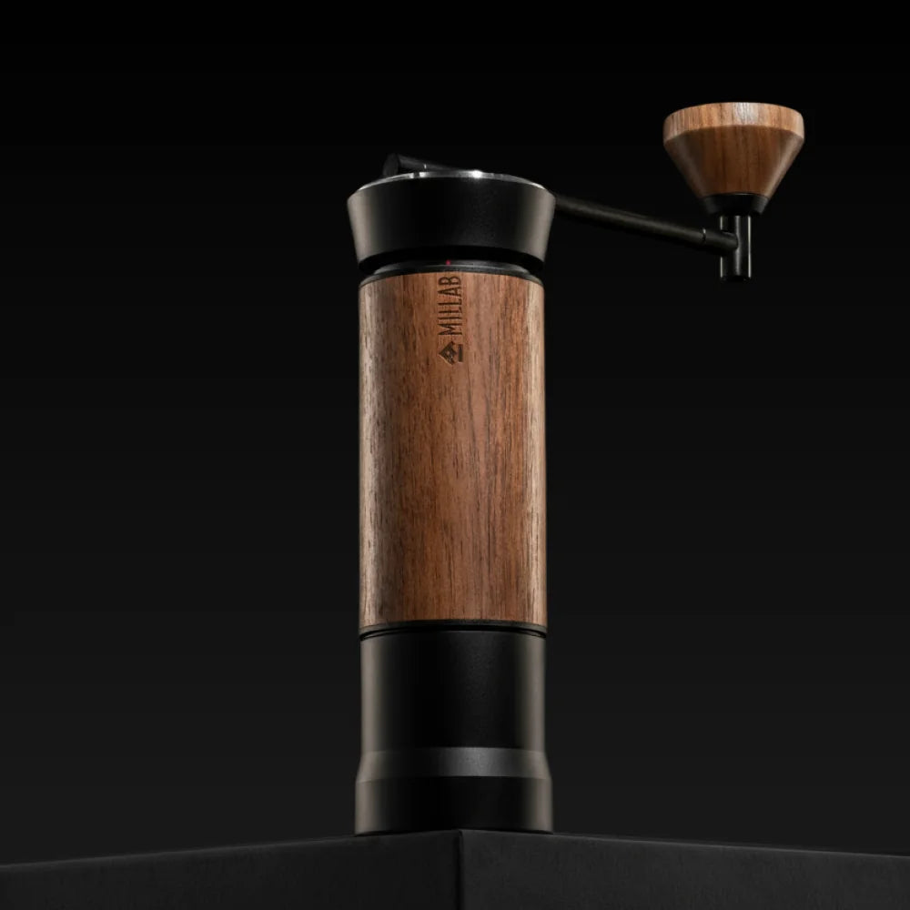 The black and walnut TIMEMORE x MILLAB M01 standing on a black plinth against a dark background, with the walnut crank knob raised