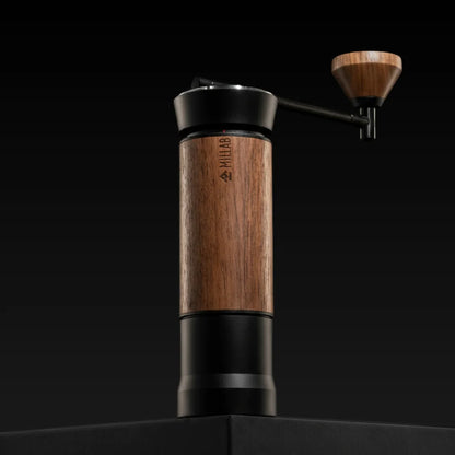 The black and walnut TIMEMORE x MILLAB M01 standing on a black plinth against a dark background, with the walnut crank knob raised