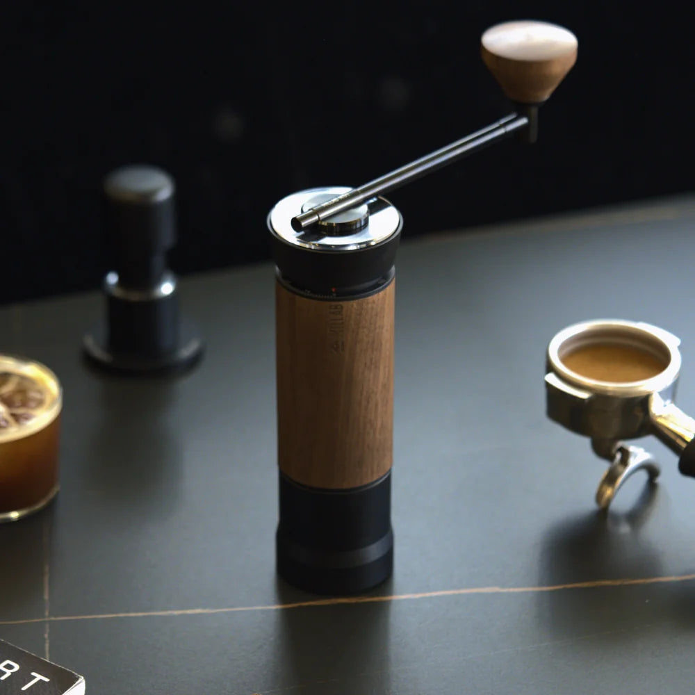 The M01 with walnut grip on a dark espresso bar next to a tamper and a portafilter holding a pulled shot
