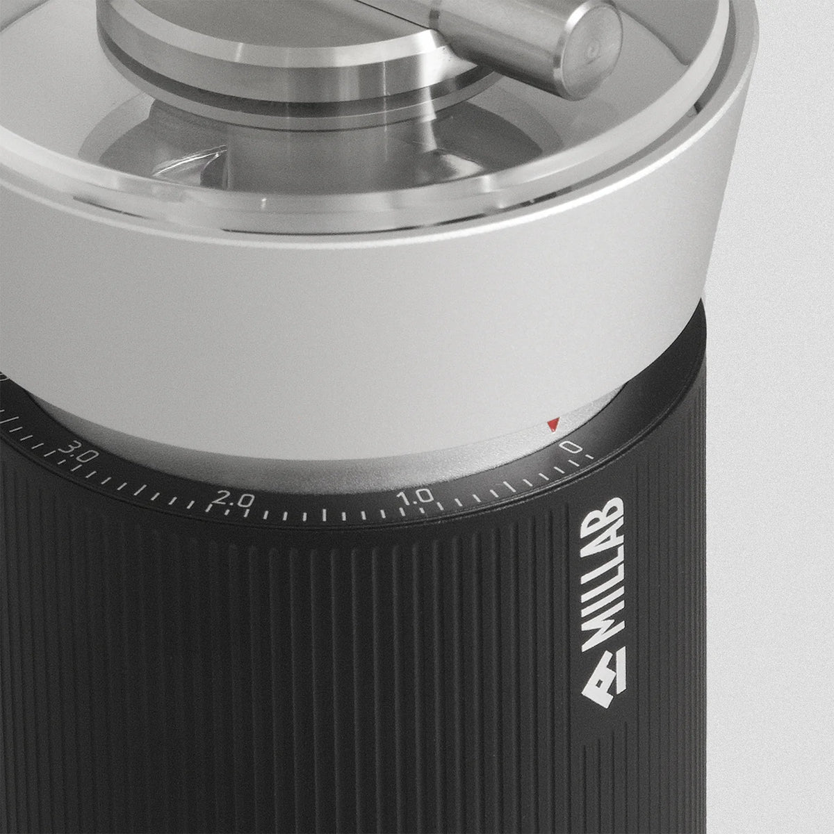 Close-up of the M01 external grind adjustment dial with its numbered scale and red index mark, above the striated black grip carrying the MILLAB logo