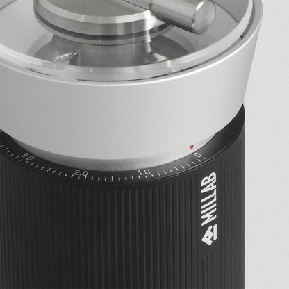 Close-up of the M01 external grind adjustment dial with its numbered scale and red index mark, above the striated black grip carrying the MILLAB logo
