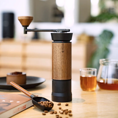 The black and walnut TIMEMORE x MILLAB M01 on a wooden table next to a cup of coffee, a scoop of beans and a glass server