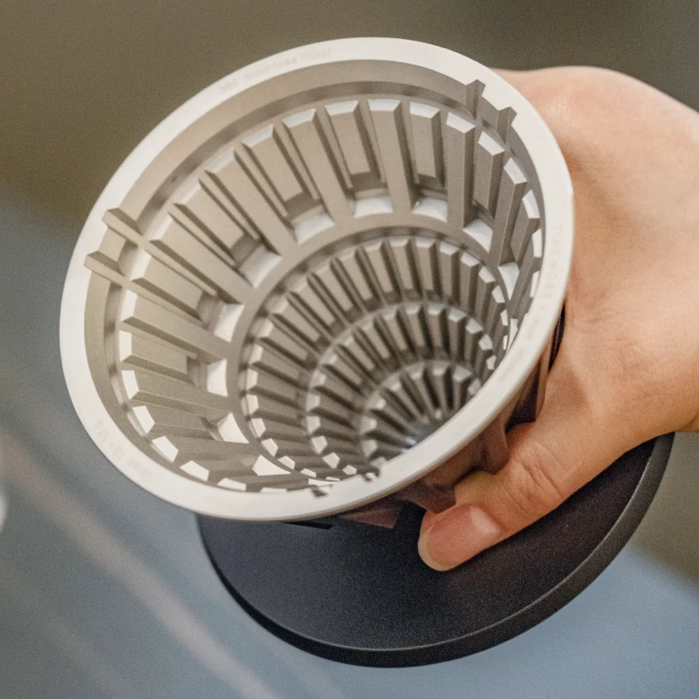 Hand holding the TIMEMORE VECTOR dripper tilted to show the staggered stainless steel lattice inside the cone