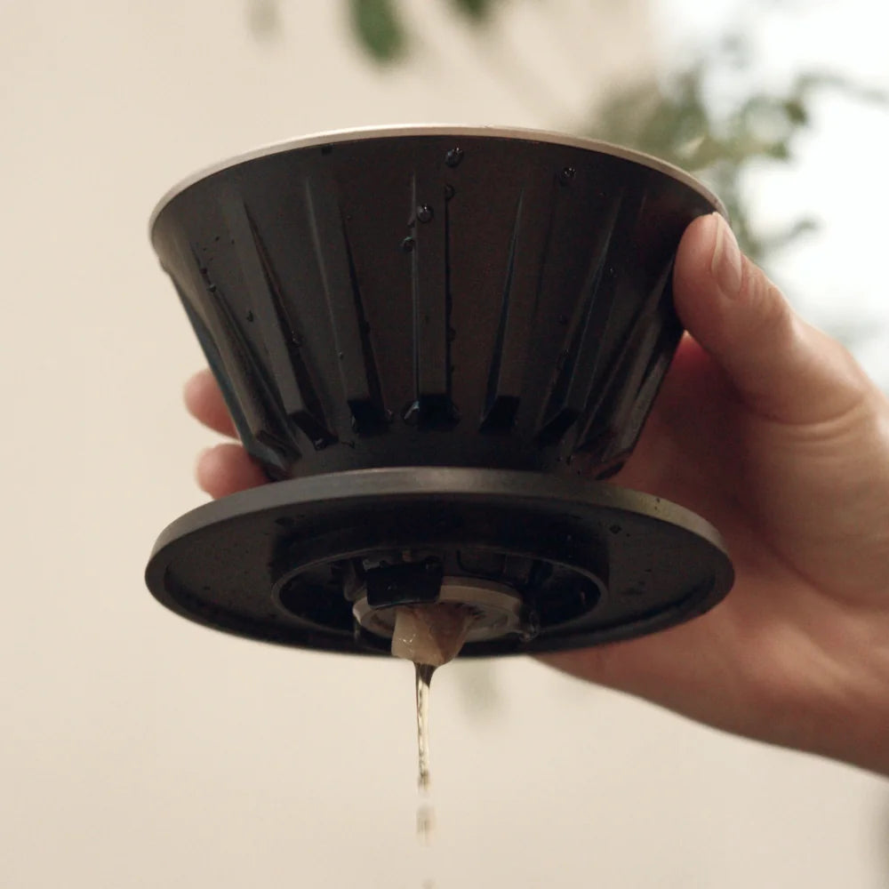 Hand lifting the black VECTOR dripper to show the base and the single outlet with coffee still dripping