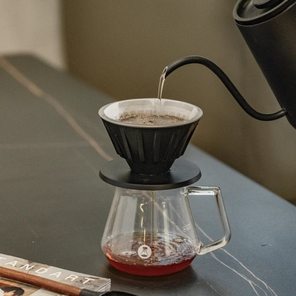 Pouring water from a gooseneck kettle into the VECTOR dripper sitting on a glass server of filter coffee