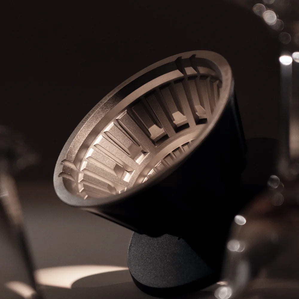 The VECTOR dripper tilted on a dark counter, light catching the stainless steel Brewer Core