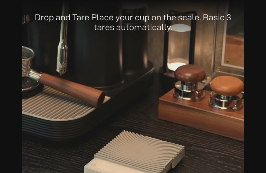 Drop and Tare: a glass cup placed on the white Basic 3 on an espresso machine drip tray — 'Place your cup on the scale. Basic 3 tares automatically.'