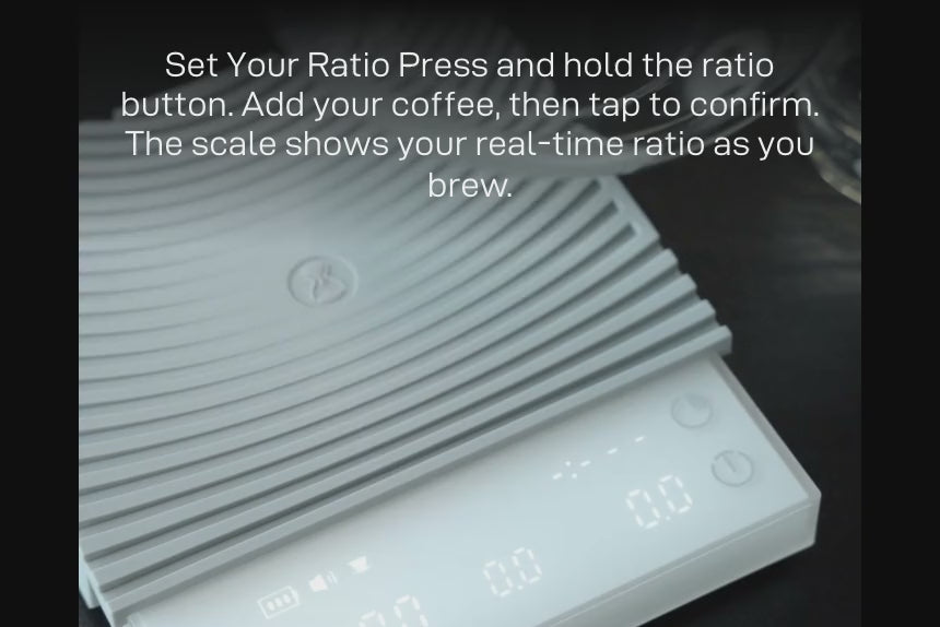Set Your Ratio: a server on the white Basic 3 while the display shows the live ratio — 'Press and hold the ratio button. Add your coffee, then tap to confirm. The scale shows your real-time ratio as you brew.'